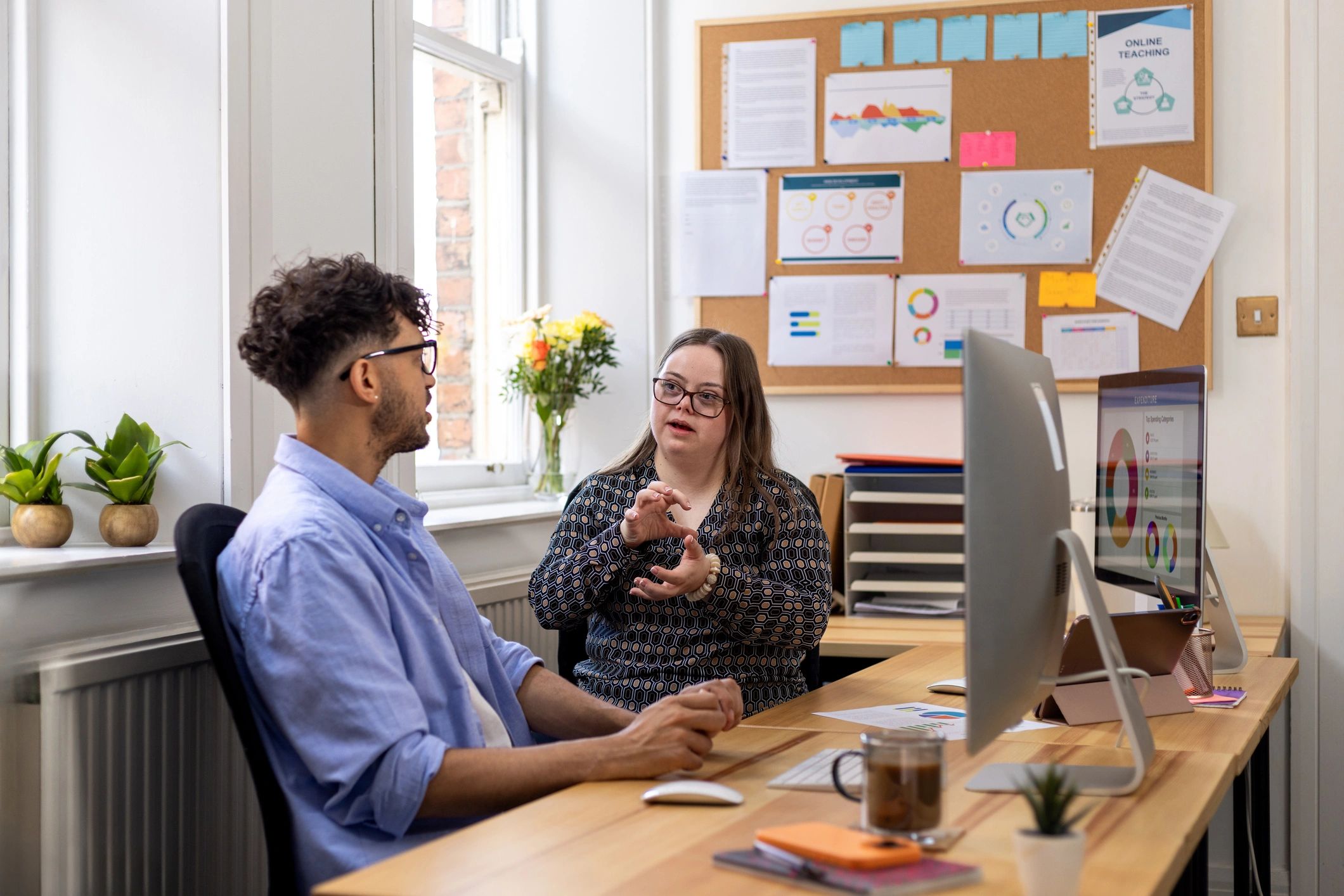 Two professionals in a coaching-style conversation at a desk